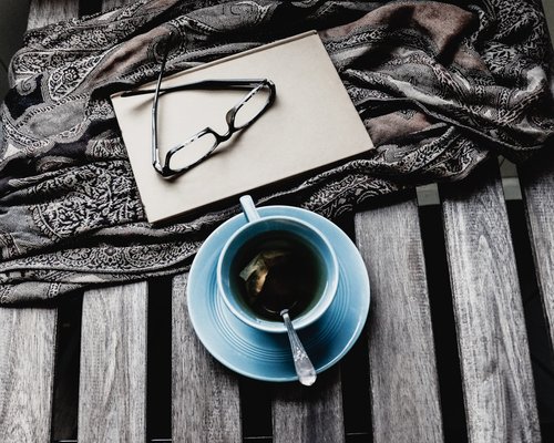 A notebook and a cup of tea on a wooden table catching the morning light
